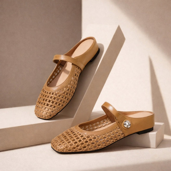 Woman wearing woven flat mules with a simple dress on a plain background.