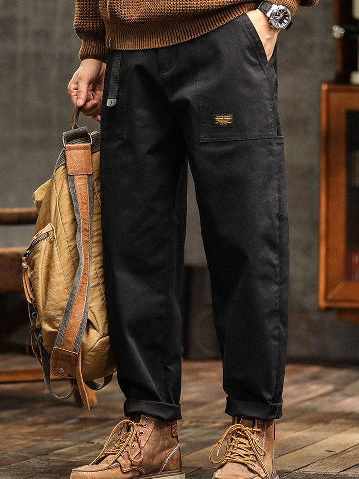 Male model wearing casual workwear-style pants with side utility pockets against a plain background.