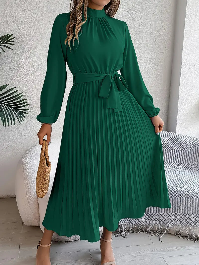 Female model in a modest long sleeve dress with pleated skirt on a plain background.