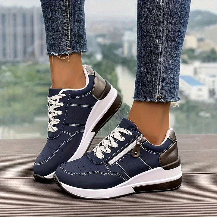Woman wearing white walking sneakers on a plain background.