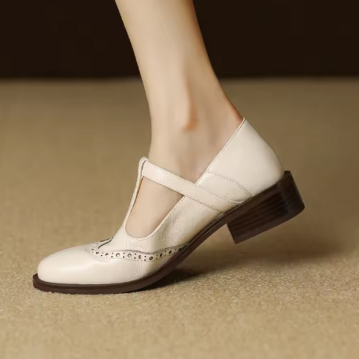 Woman wearing textured flat mules with strap detail on a plain background.