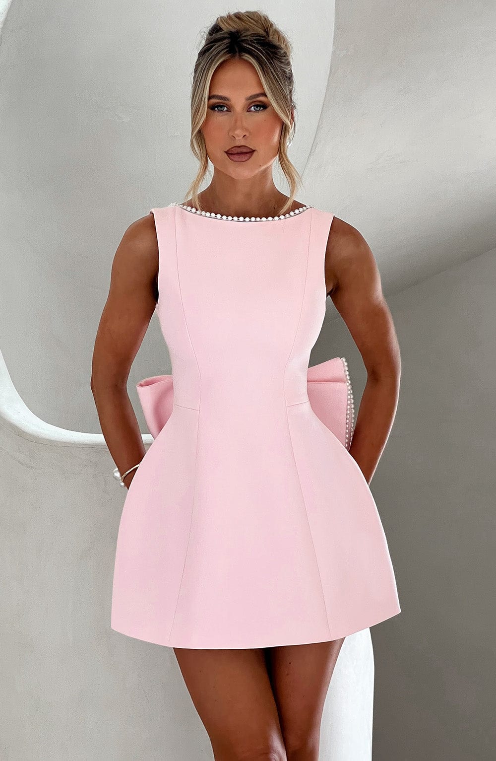 Female model wearing structured mini dress on plain gray background.