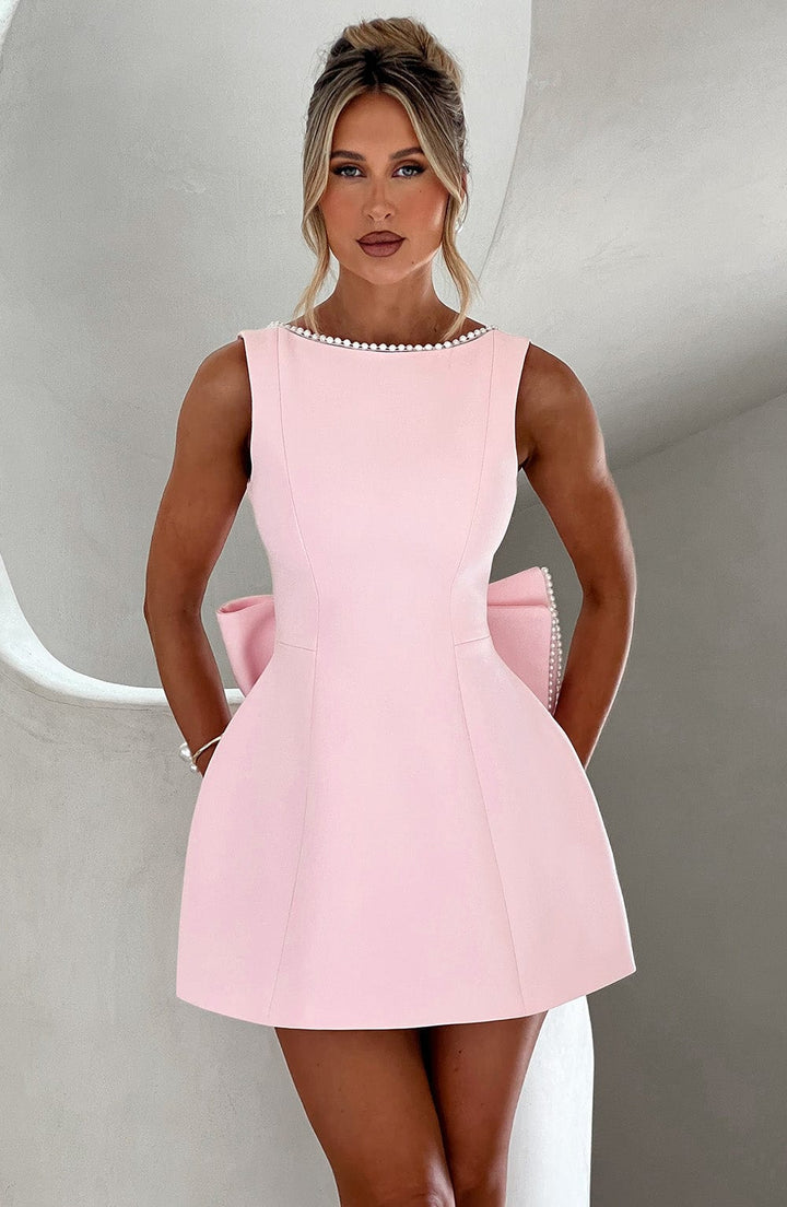 Female model wearing structured mini dress on plain gray background.