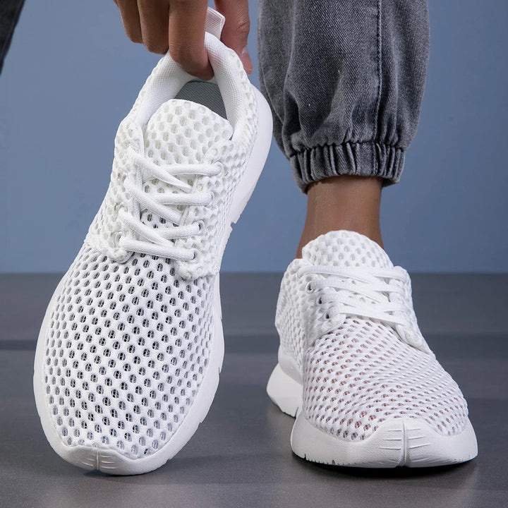 Female feet styled in lightweight everyday sneakers with a plain backdrop.