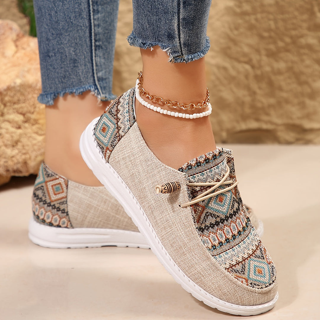 Feet wearing tribal print women’s sneakers on a plain background.