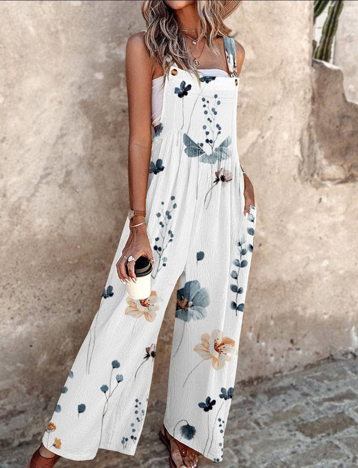  Woman showcasing a sleeveless floral jumpsuit with a flowing wide-leg design on a plain background.
