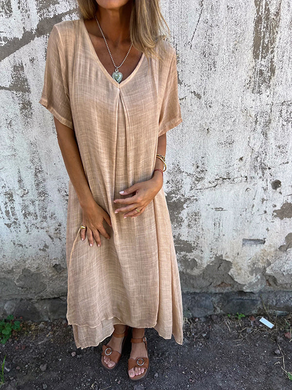 Woman posing in a full-length elegant dress with soft draping on a plain backdrop.