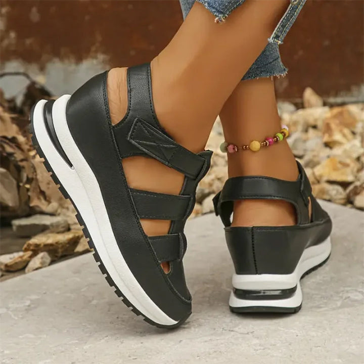 Woman showing feet in strap-detail sneakers against a plain background.