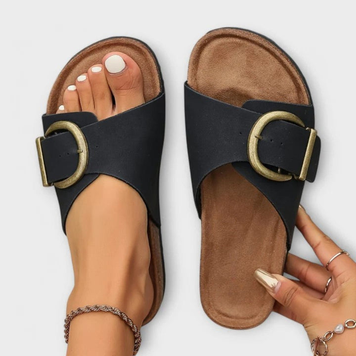 Female model wearing stylish open-toe sandals on a plain background.