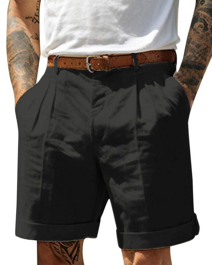 Man showcasing high-waisted chino shorts with cuffed hem on a plain background.