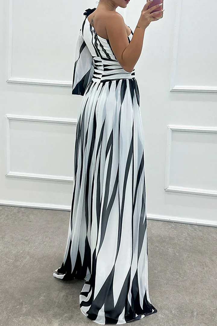 Woman showcasing an asymmetrical striped maxi dress with a plain background.