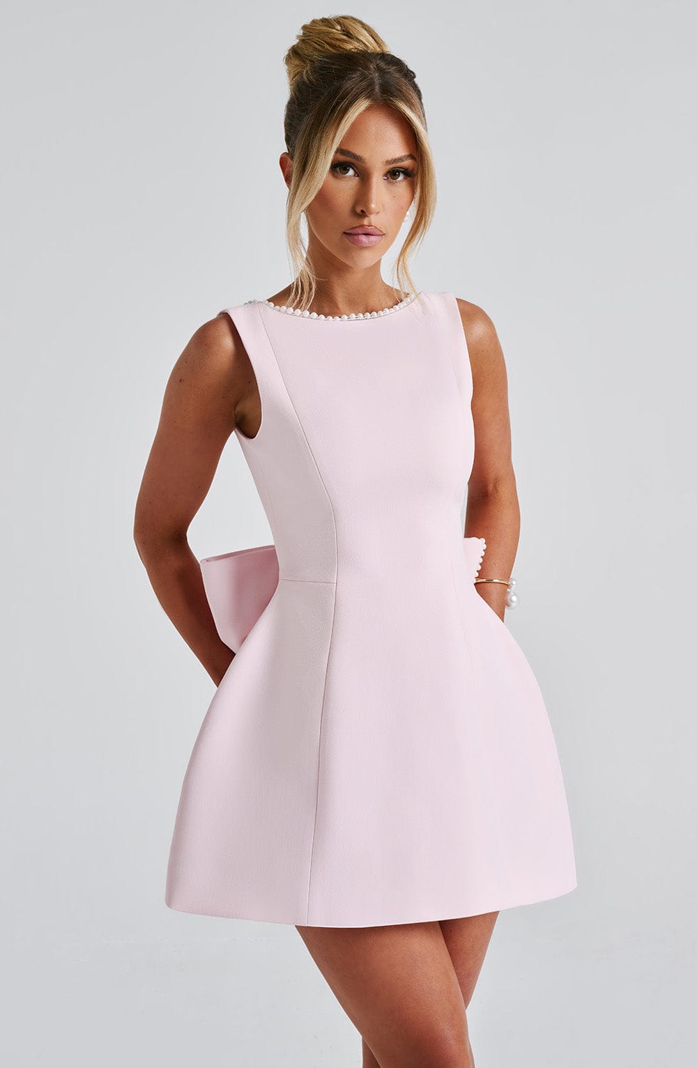 Woman posing front view in tailored mini dress, gray background.