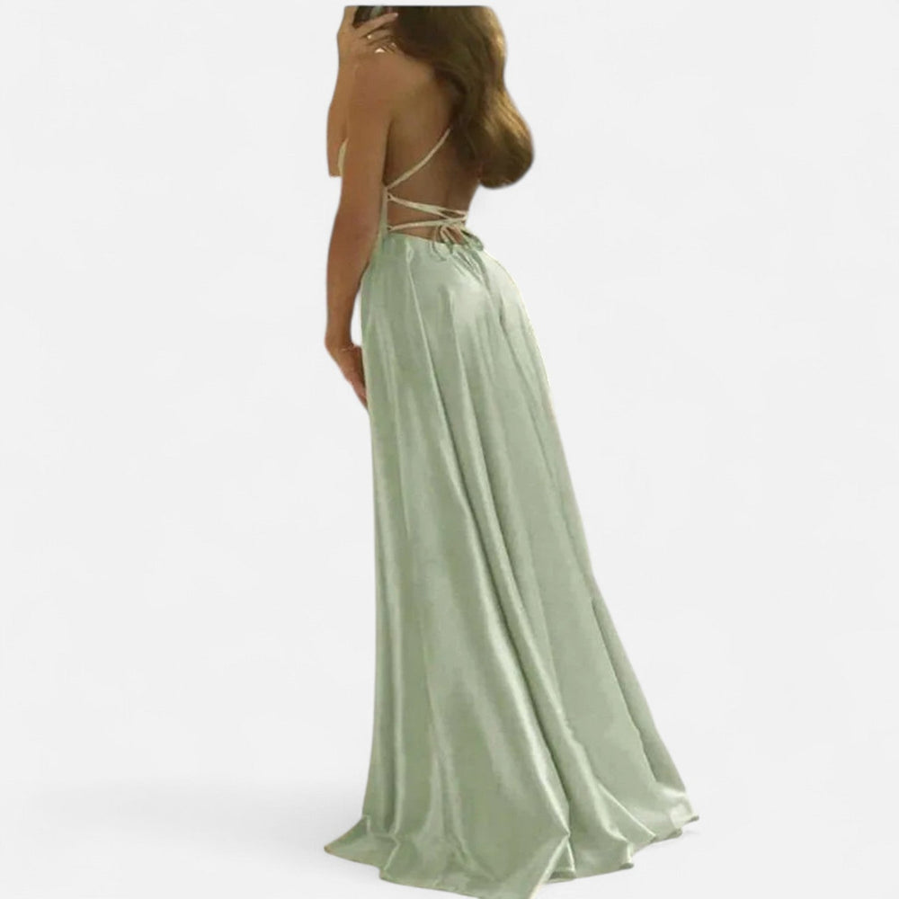 Woman posing in flowing maxi dress with side slit, plain background.