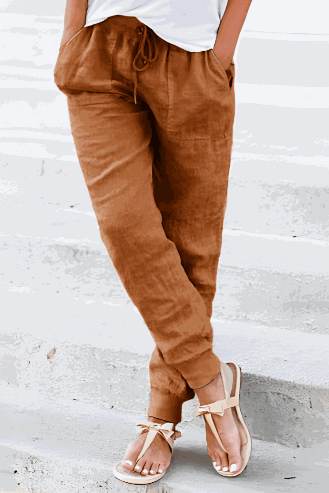 Woman styling drawstring waist pants with sandals on a clean background.