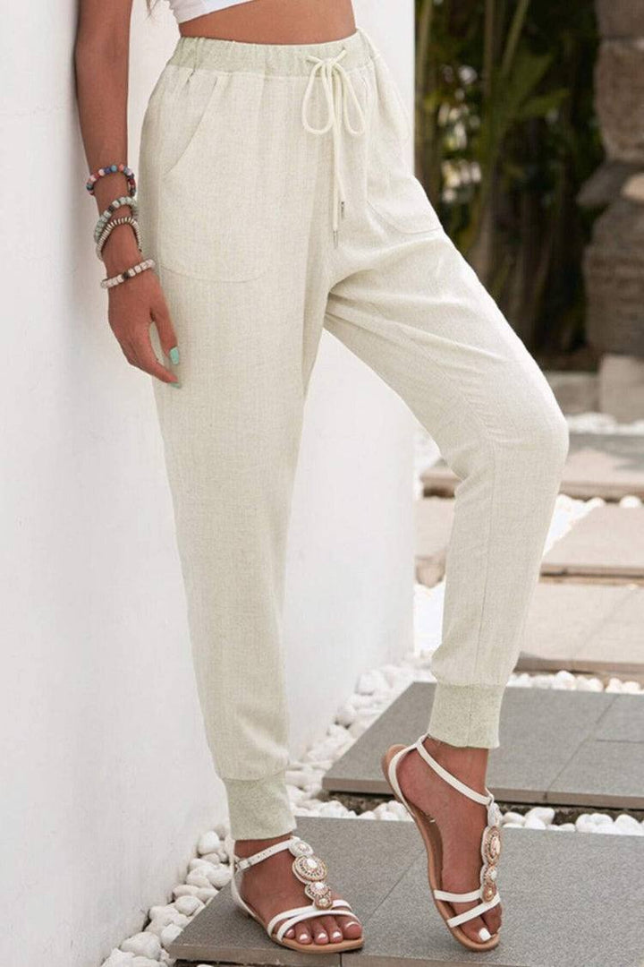 Woman styling casual drawstring pants with side pockets on a plain background.