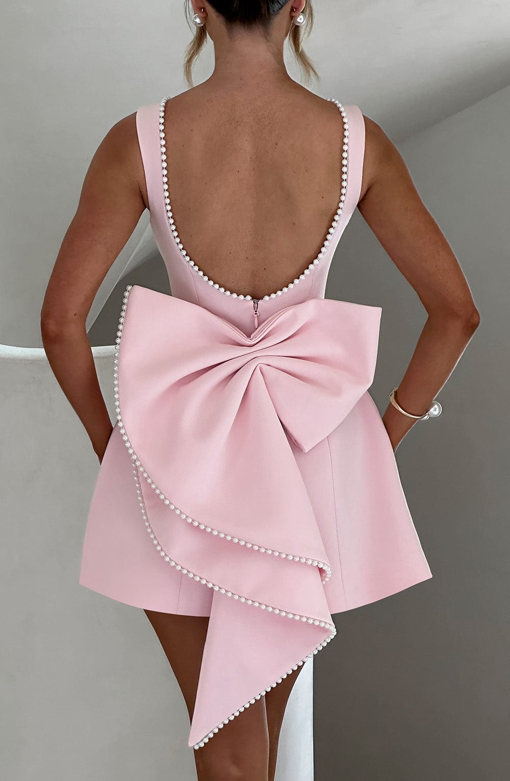Female model showing back angle of elegant mini dress, gray.