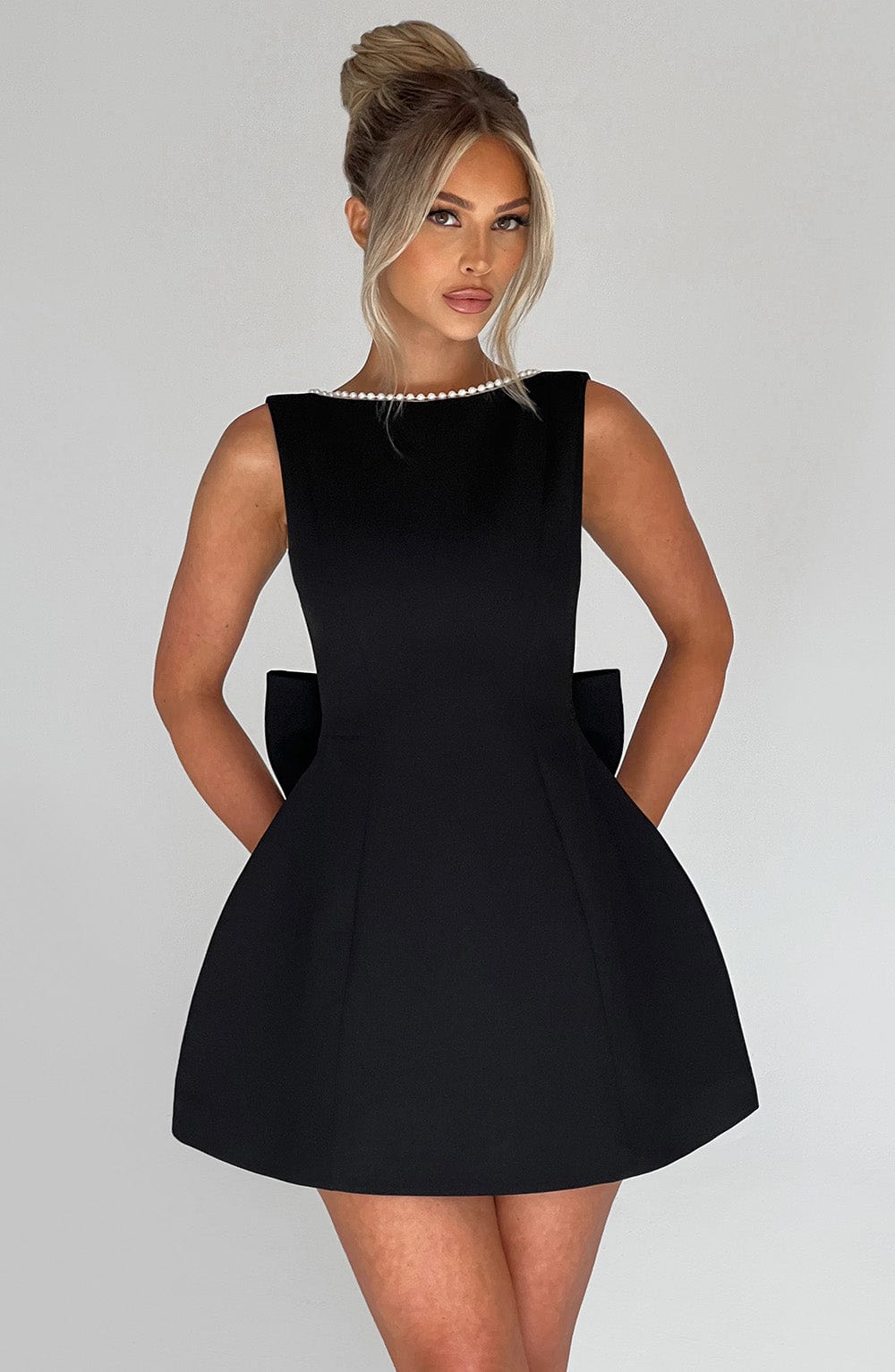Woman in structured occasion dress with plain gray studio background.