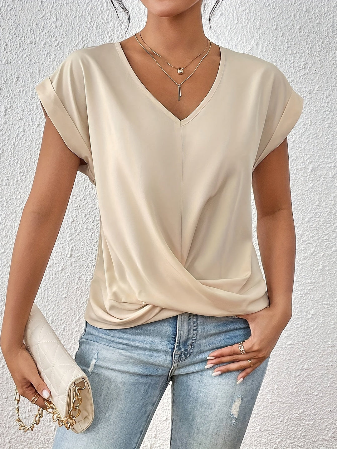 Woman slight side angle holding clutch wearing cream top, gray simple background
