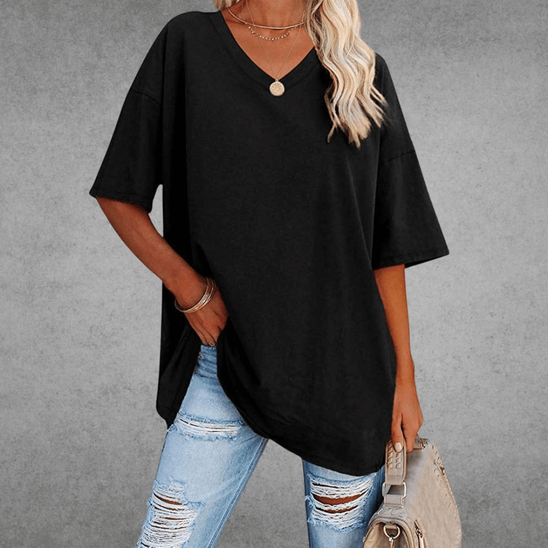 Woman wearing oversized V-neck shirt, holding bag, gray plain background.