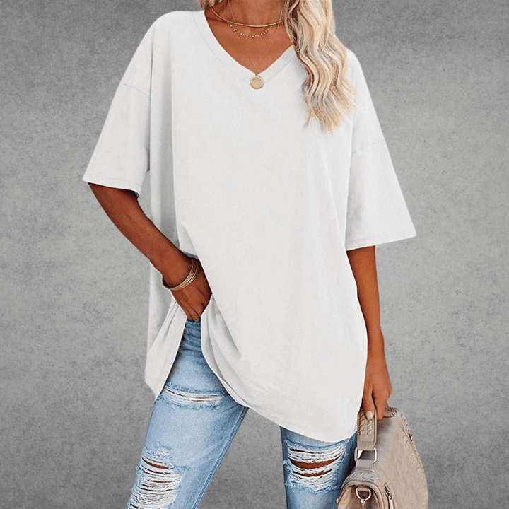 Woman styling casual V-neck shirt with bag, plain gray background.
