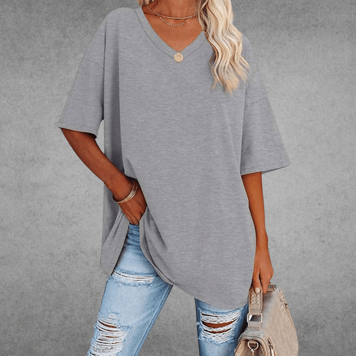 Woman wearing loose shirt and holding bag, gray backdrop.