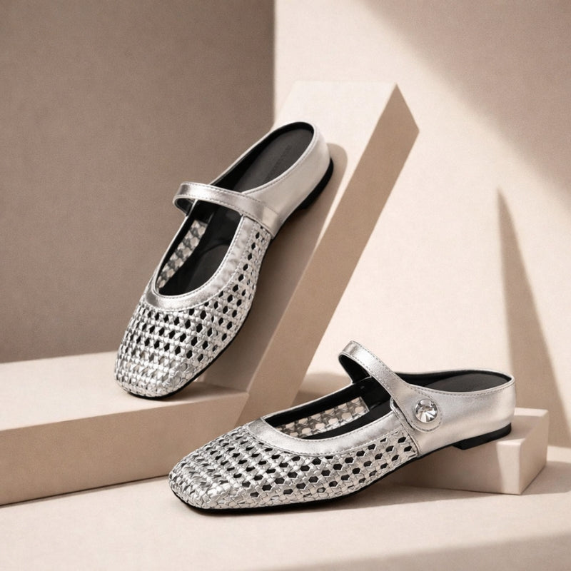 Model wearing flat mule shoes with woven texture and strap detail on a plain background.