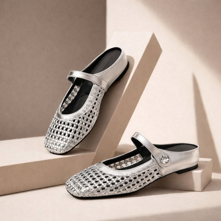 Model wearing flat mule shoes with woven texture and strap detail on a plain background.