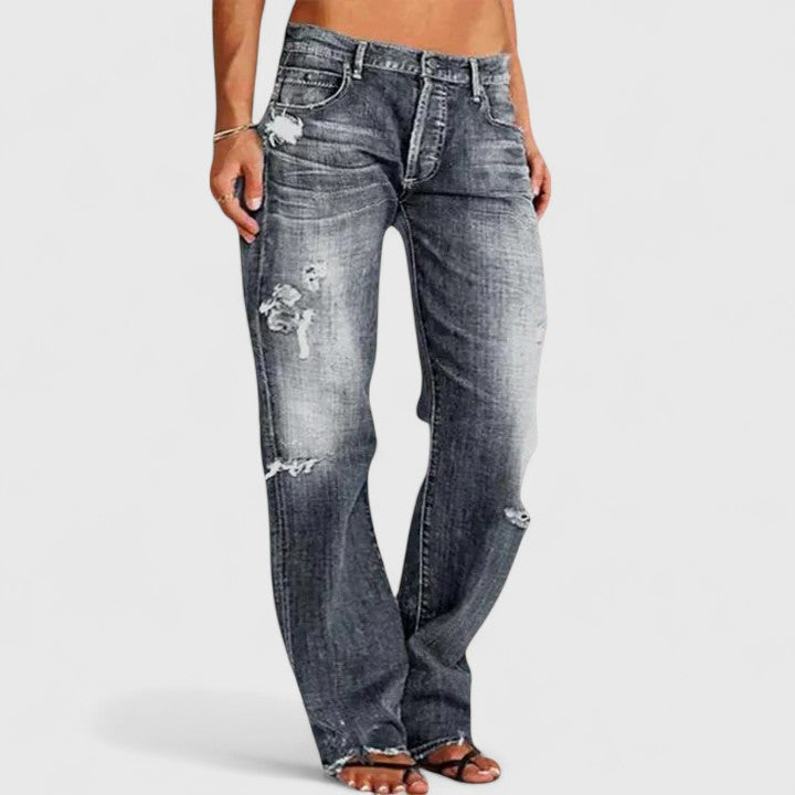 Woman styling distressed flare denim jeans on a plain background.