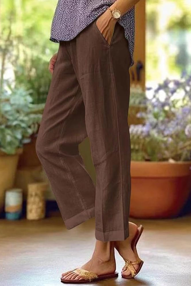 Model in casual summer trousers walking through a leafy background.