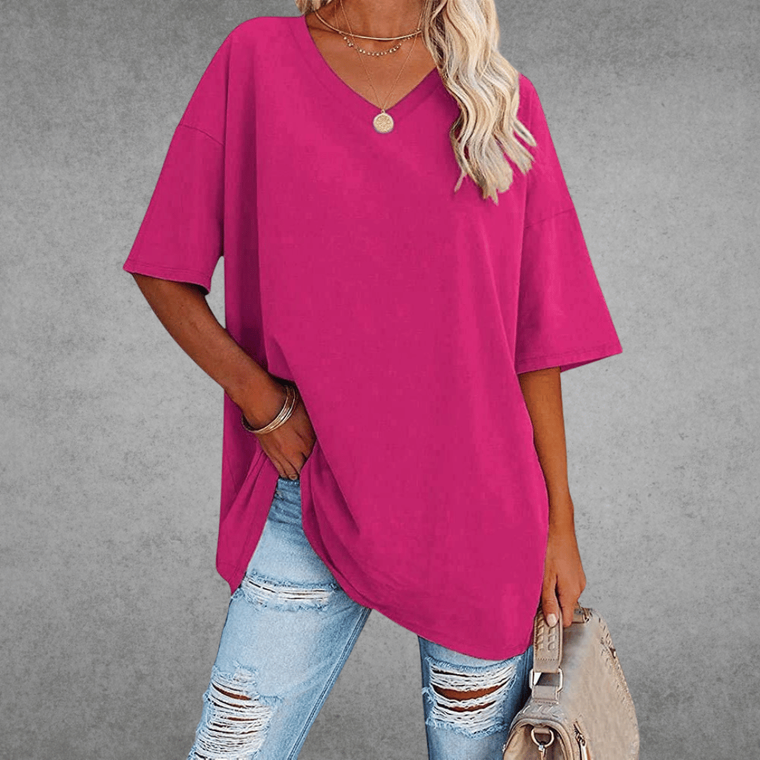 Relaxed V-neck top on woman with bag, plain gray background.