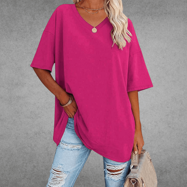 Relaxed V-neck top on woman with bag, plain gray background.