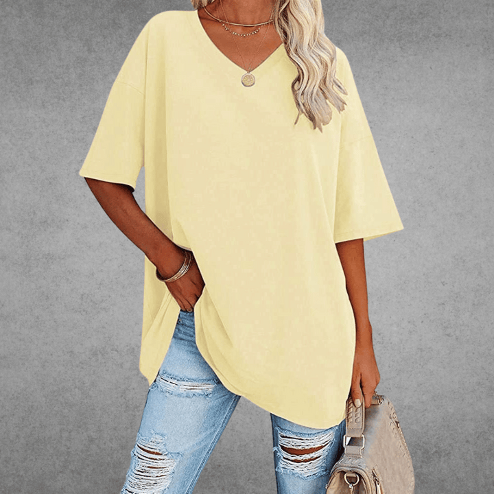 Front-facing woman in oversized top, holding bag, gray backdrop.