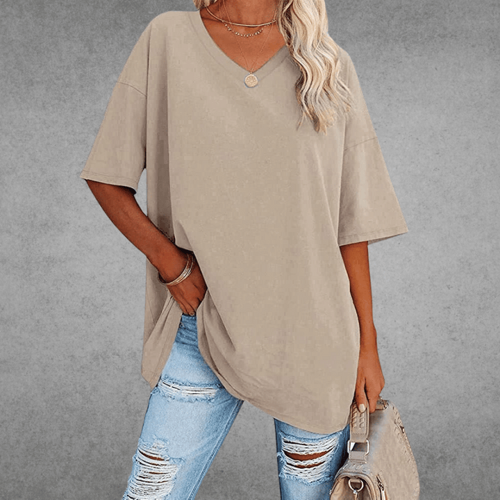 Woman carrying bag in relaxed V-neck shirt, gray background.