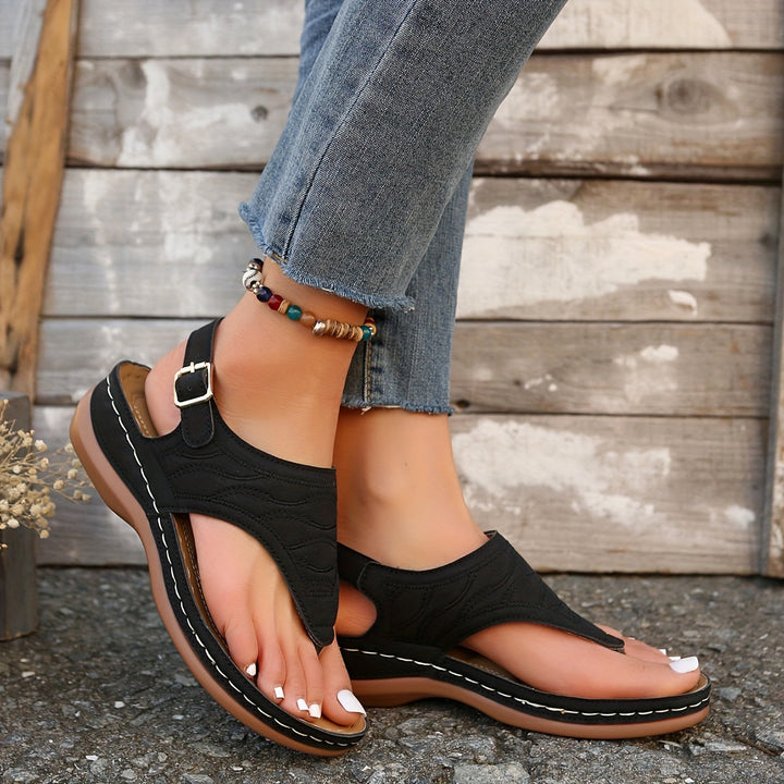 Woman standing in casual clip toe sandals against a plain background.