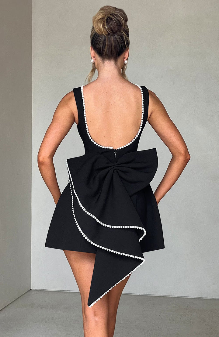 Woman displaying fitted mini dress from back angle, gray background.