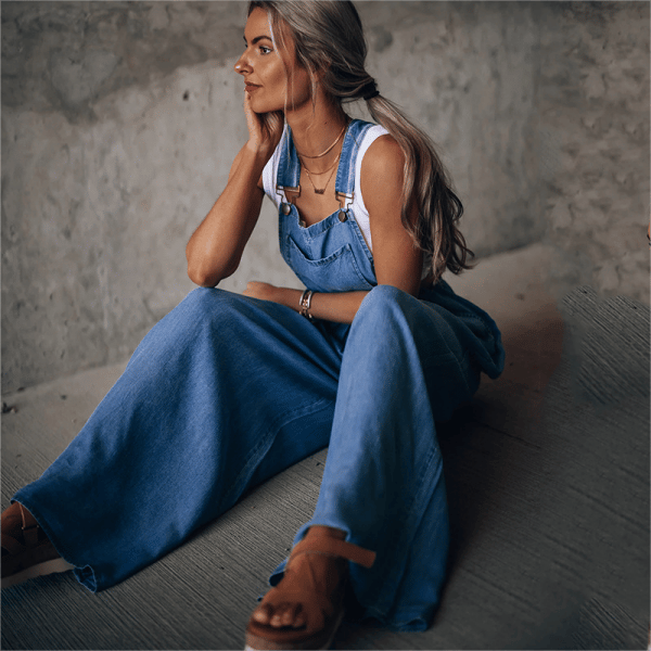 Denim dungaree jumpsuit with flowing wide-leg shape on plain background.