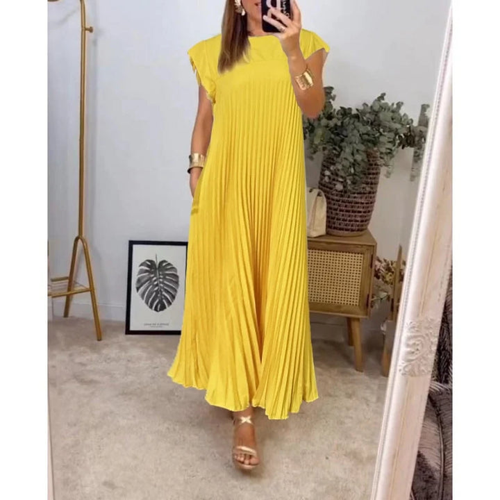 Woman standing in a soft draped maxi dress against a plain studio background.