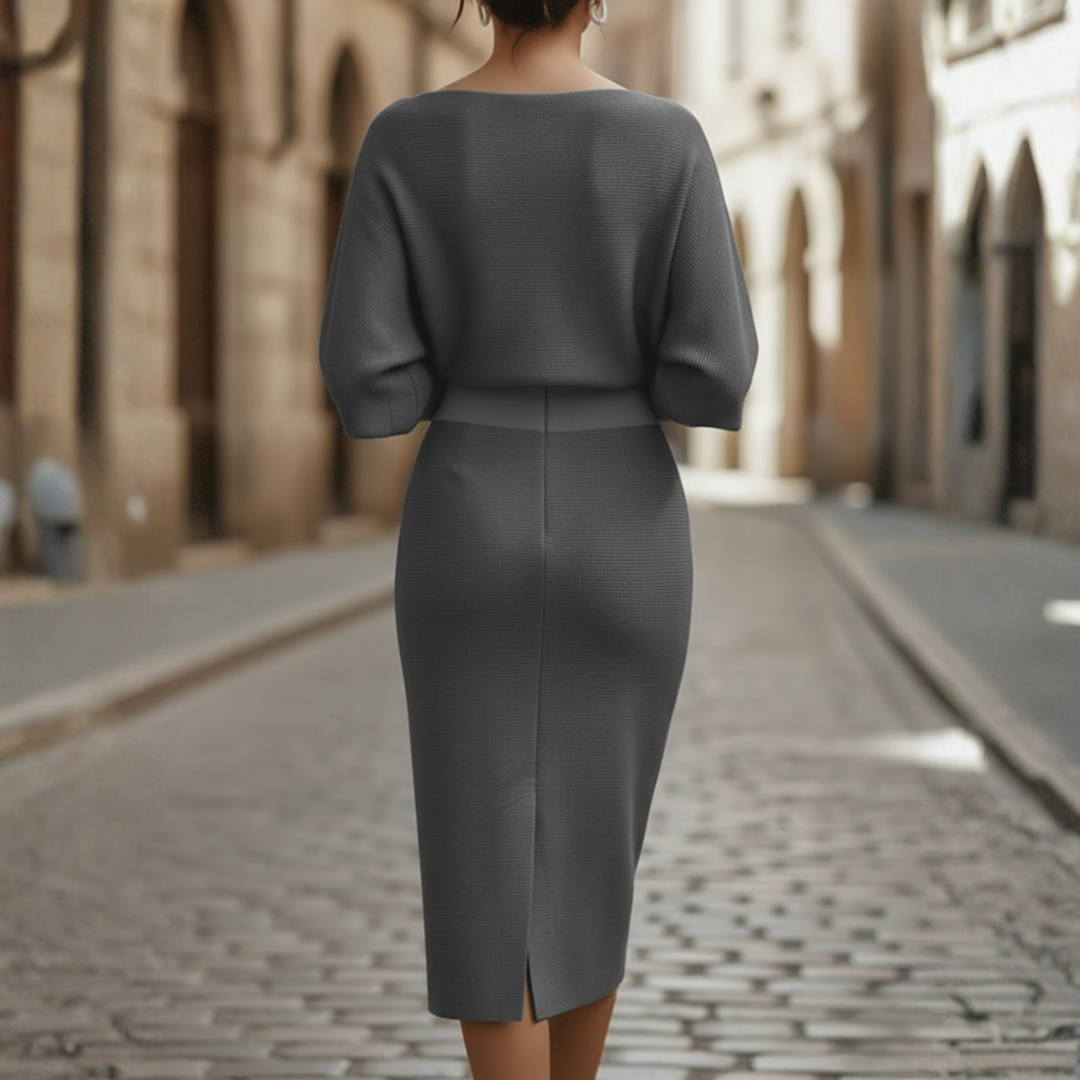 Woman styled in a draped midi dress with three-quarter sleeves and sleek fitted skirt against a plain background.