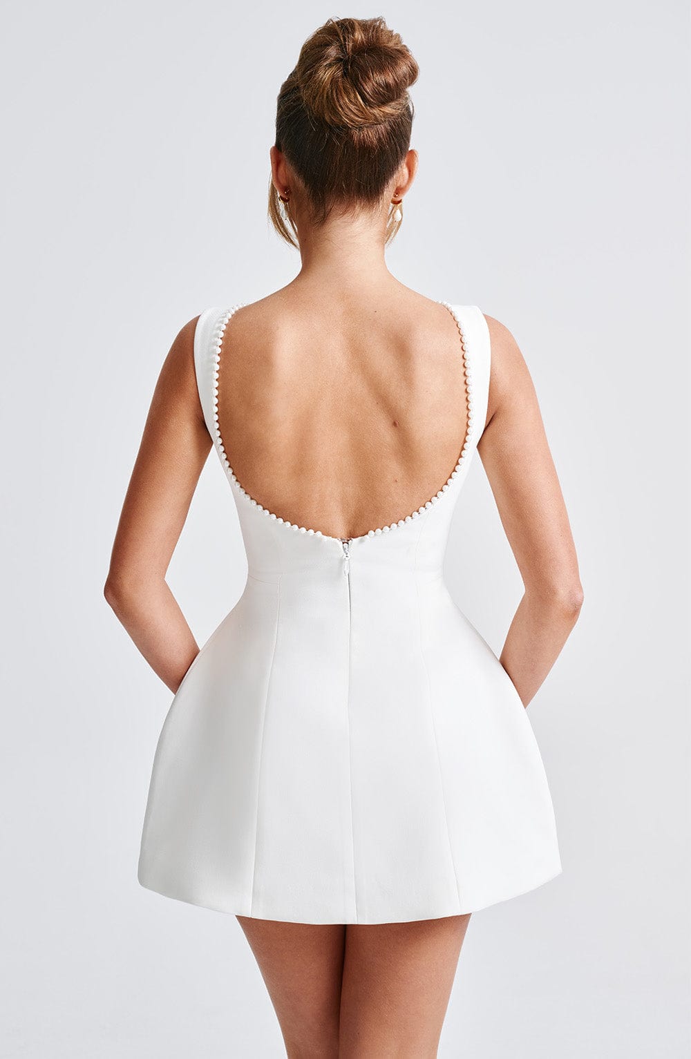Woman posing in chic structured dress, back profile, gray backdrop.