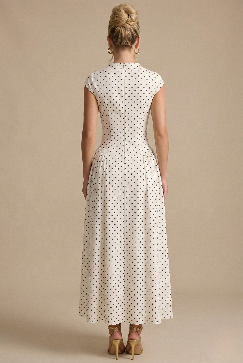 Woman showcasing a full-length polka dot dress with a defined waist and flowing skirt on a plain background.