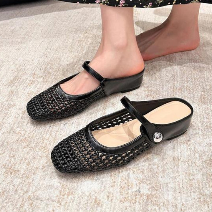 Woman wearing slip-on woven mules with strap detail on a plain background.