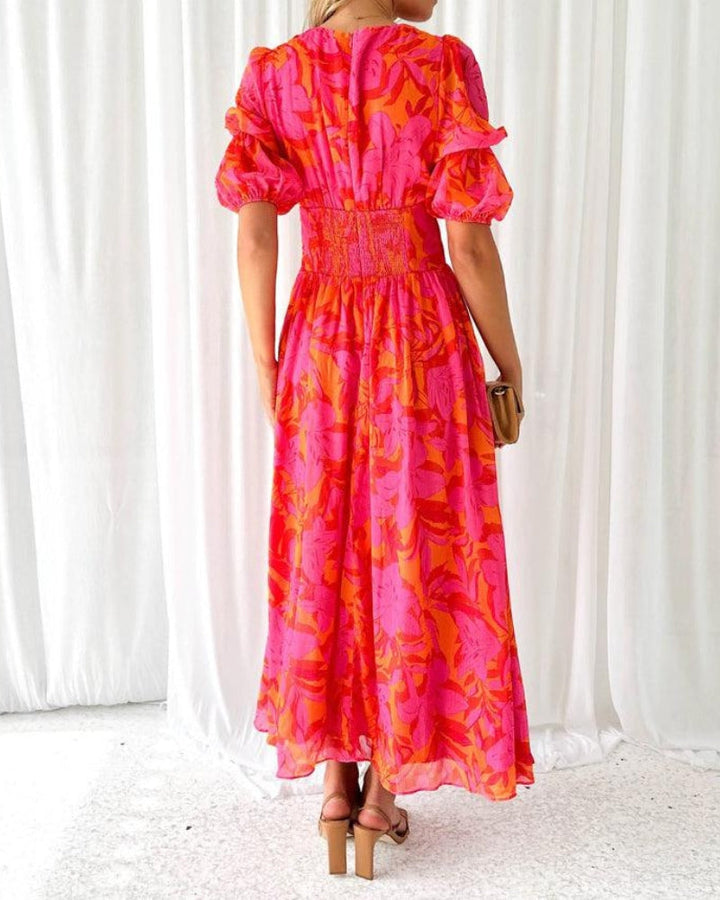 Woman showcasing a long V-neck dress with an elegant silhouette on a plain background, back view