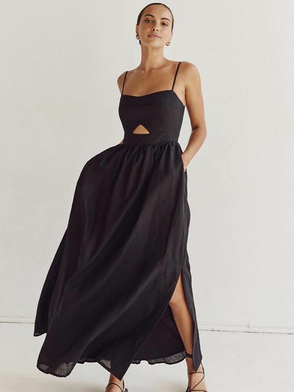 Woman showcasing a flowing sleeveless maxi dress with a graceful silhouette on a plain background.
