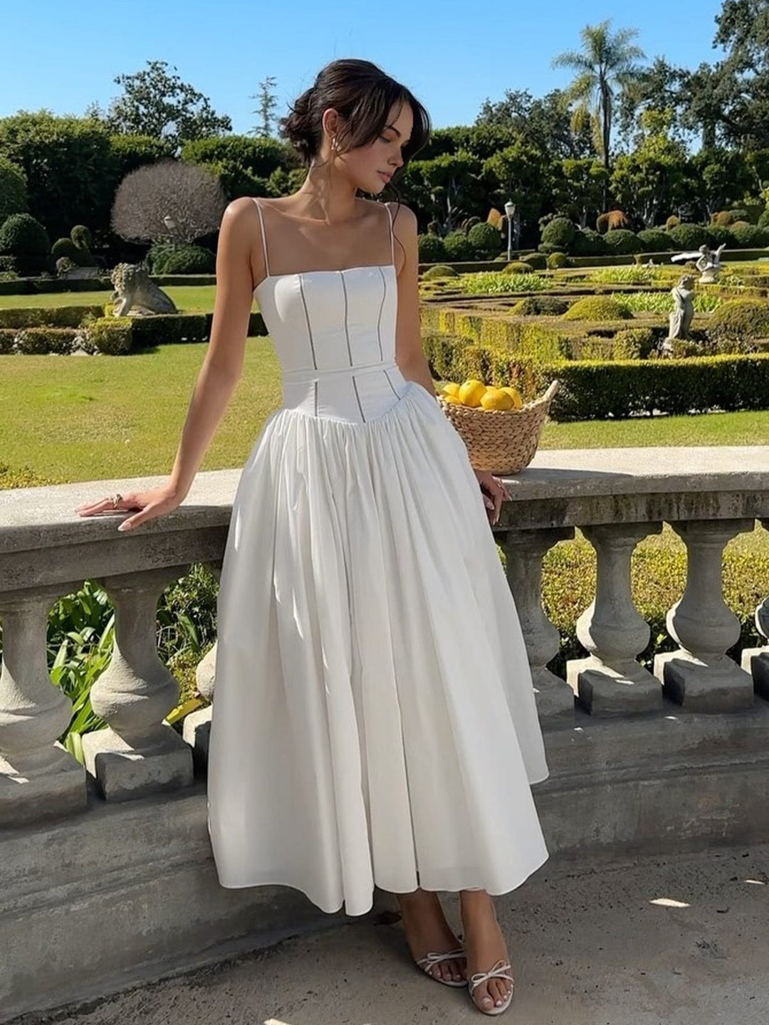 Woman posing outdoors in elegant midi dress on sunny terrace.