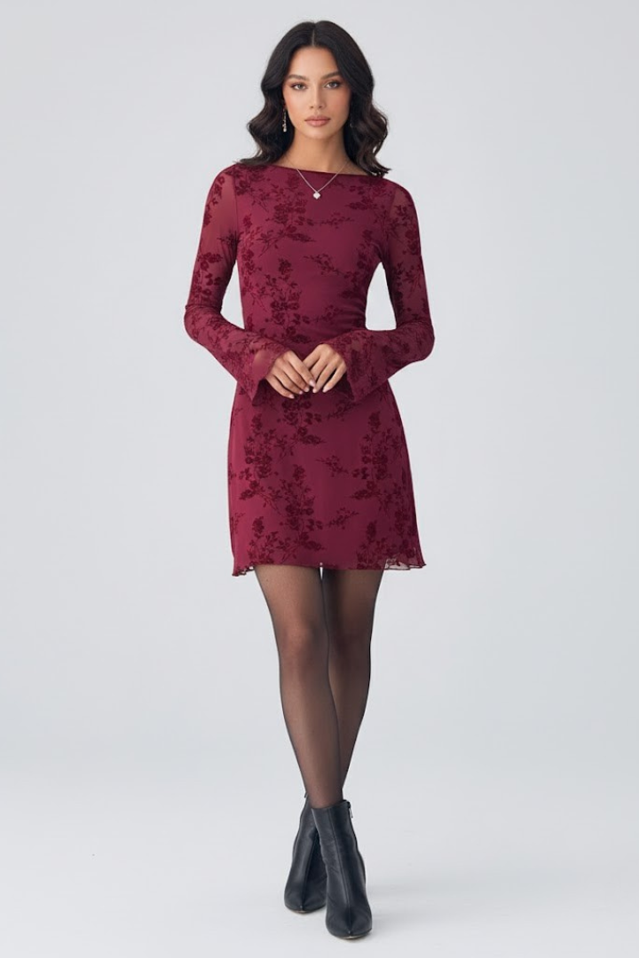  Woman modeling a sheer floral overlay mini dress with a ruched waist on a plain background.