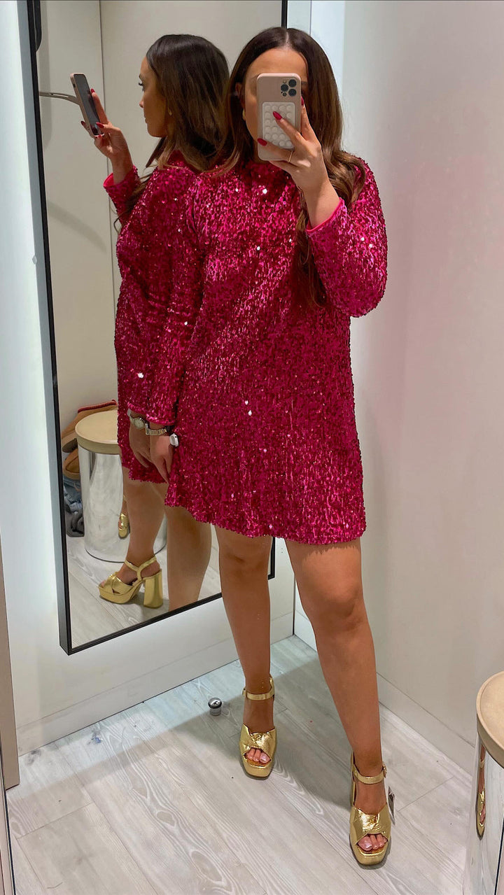 Woman posing in a long sleeve party dress with shimmering detail on a plain background.