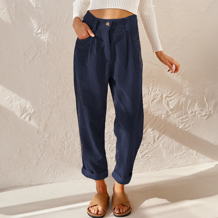 Female model showcasing pleated corduroy trousers on a plain background.