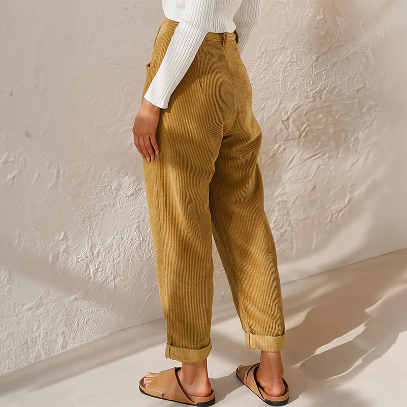 Woman showcasing relaxed fit textured trousers with front pleat details on a plain background.