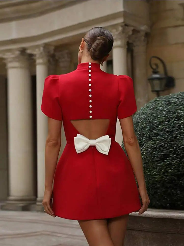  Woman in a red short sleeve mini dress with bow accent on a plain background.
