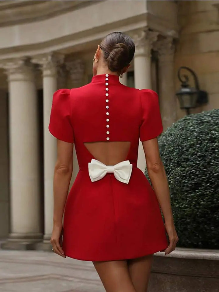  Woman in a red short sleeve mini dress with bow accent on a plain background.